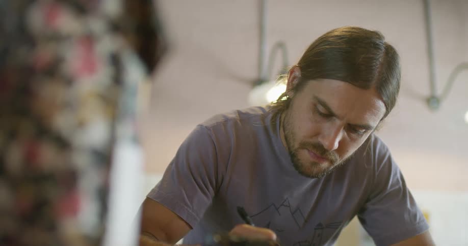 Man leans over surface writing with pen