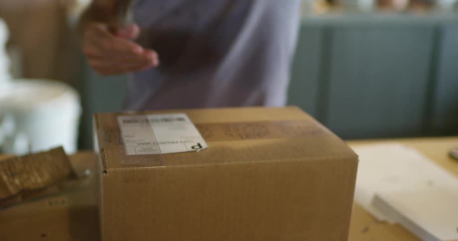Man taping a label on a cardboard box over a desk inside a small warehouse