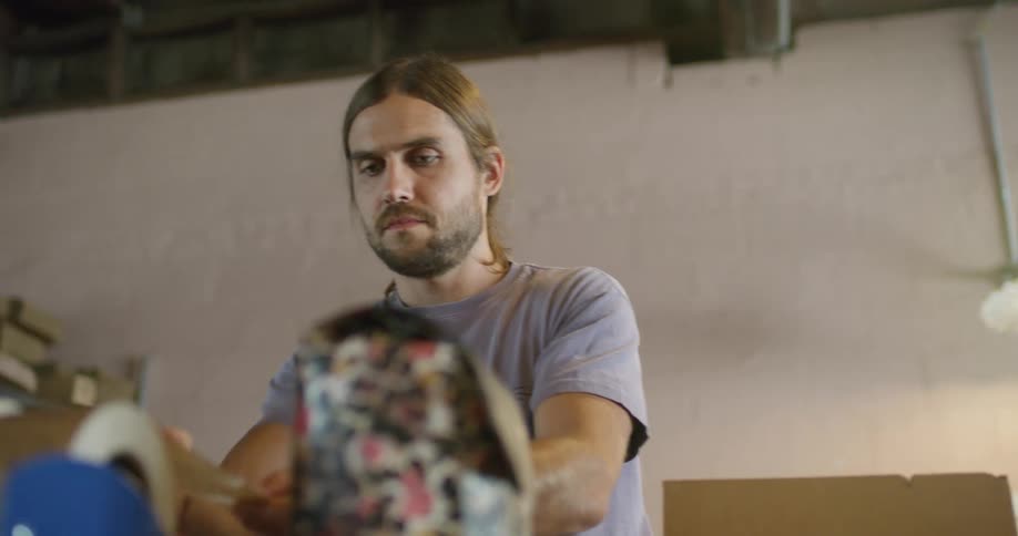 A man systematically packs a cardboard box and tapes it up