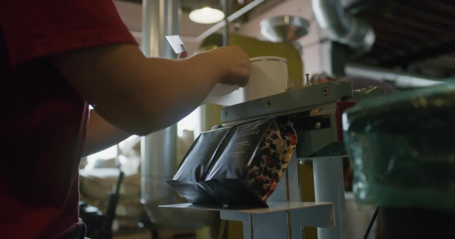 A factory employee places a sticker on a bag of coffee