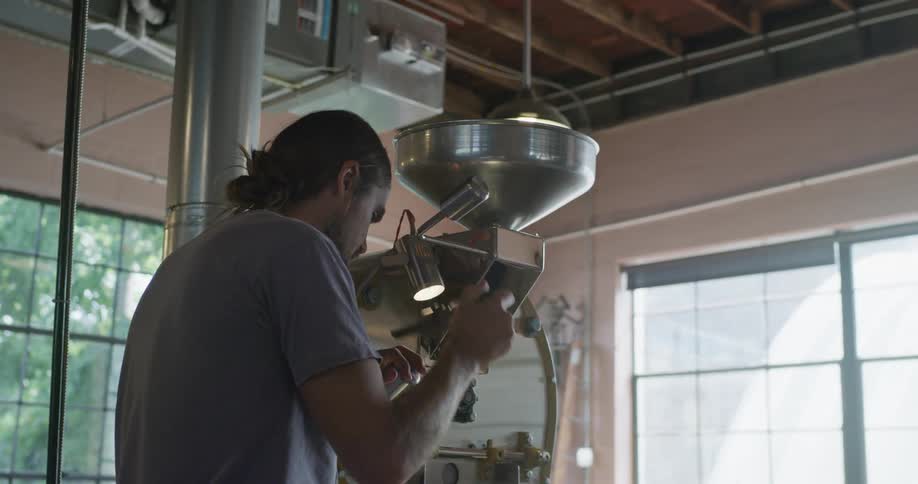 Man operates coffee roasting machine smelling the product briefly