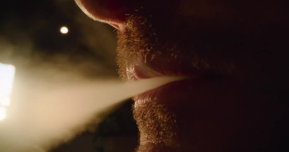 Man exhales smoke while outdoors at night in the dark