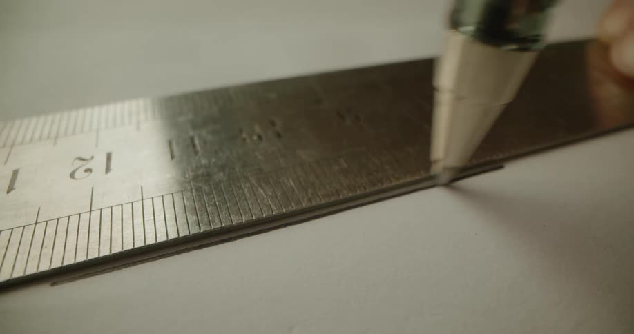 A pen drawing a line on paper using a metal ruler