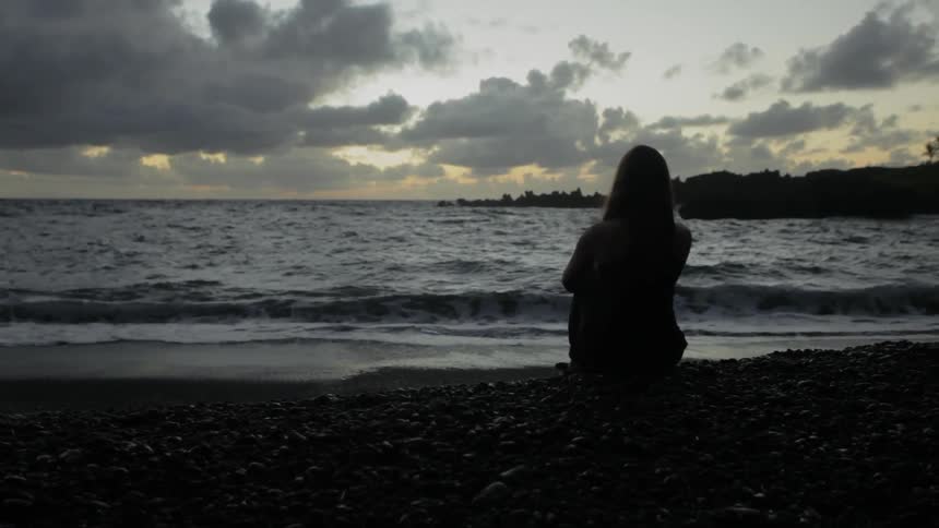 A woman sits on the ground near the water's edge