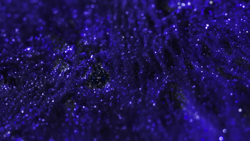 Purple glitter rises from black material and shimmers in a microscopic scene
