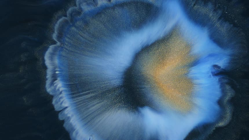 a drop of golden and white ink unfolds on dark blue background