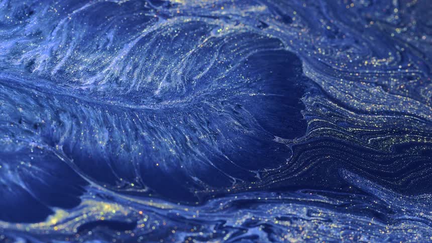 A blue liquid flows and explodes and gold glitter shimmers through the pattern