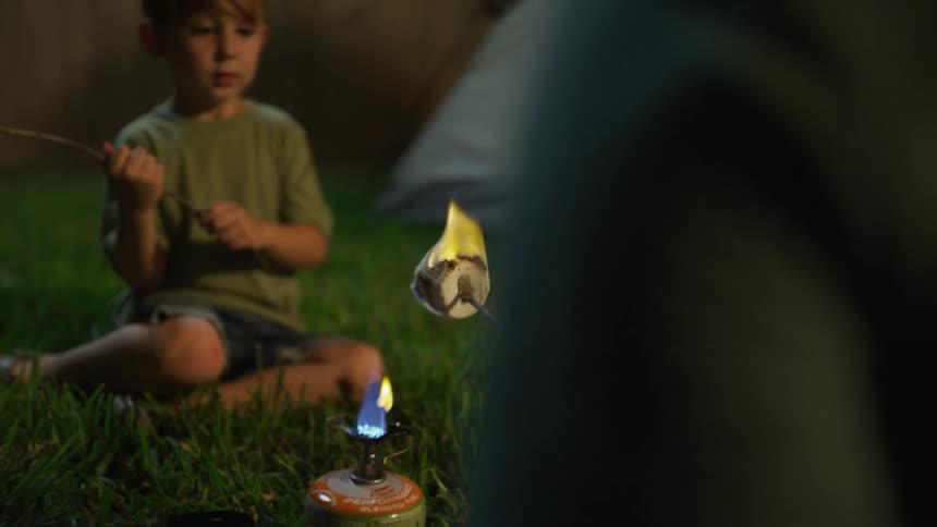 Father and son camp in backyard roasting marshmallows over camp stove