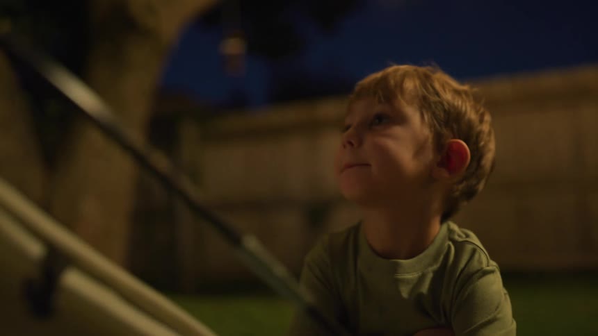 A boy and a backyard adjusting a tent with a fence a tree and the sky in the background