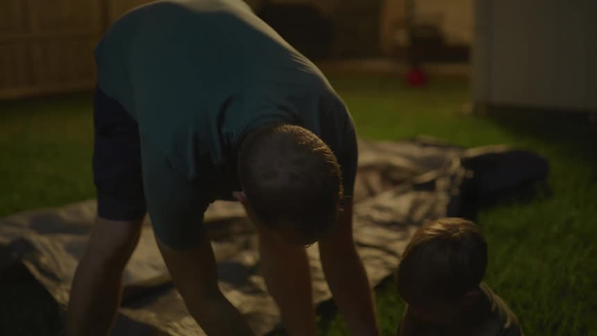 Father and son assembling a tent on the backyard at night