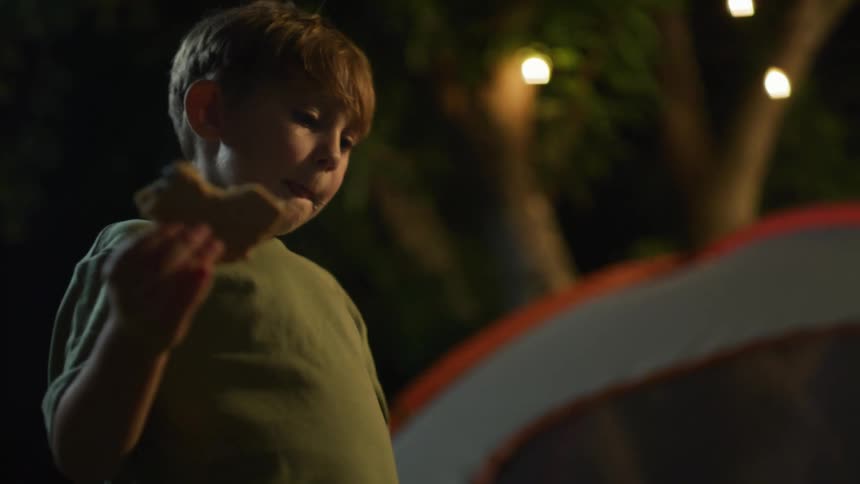 Boy eating a sandwich while camping on the backyard at night