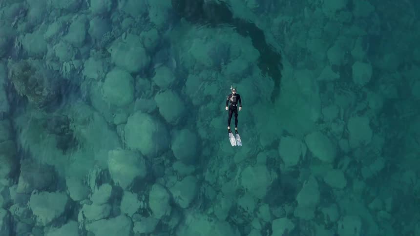 A scuba diver in a wetsuit floating on their back while swimming in turquoise ocean waters