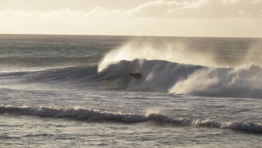 Young man riding a surfboard over a wave in the ocean at sunset
