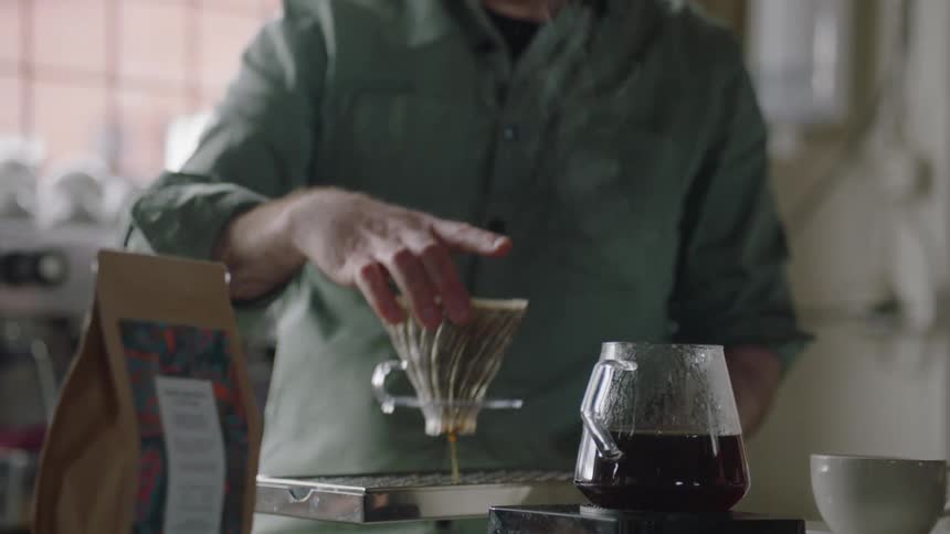 Barista lifts the filter of a brewing coffee pot over the counter top on a restaurant