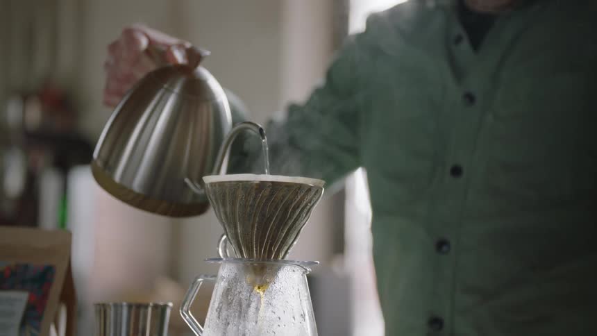 A man pours hot steaming water through a filter into a glass coffee carafe