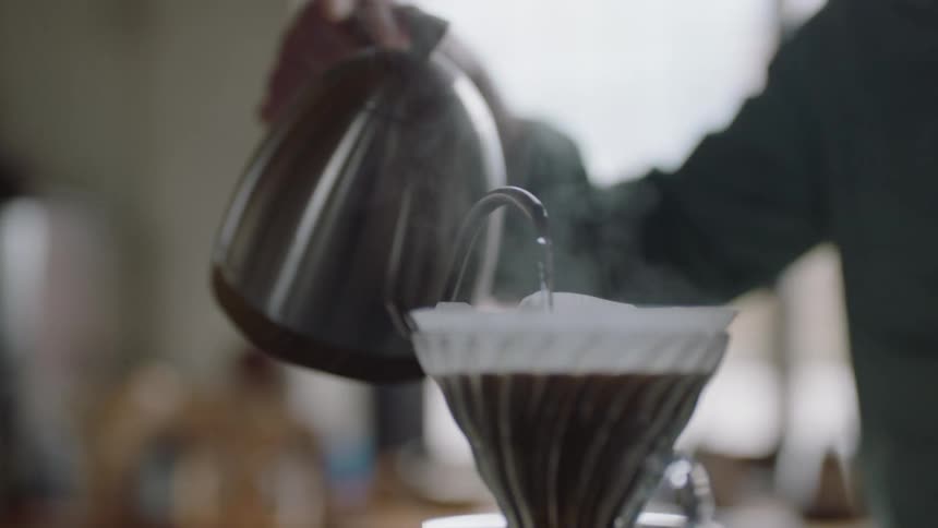 A man pours water from a kettle on coffee grounds in a pour over coffee maker