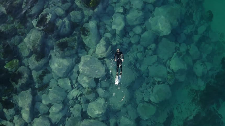 A scuba diver floating on their back while swimming in turquoise ocean water