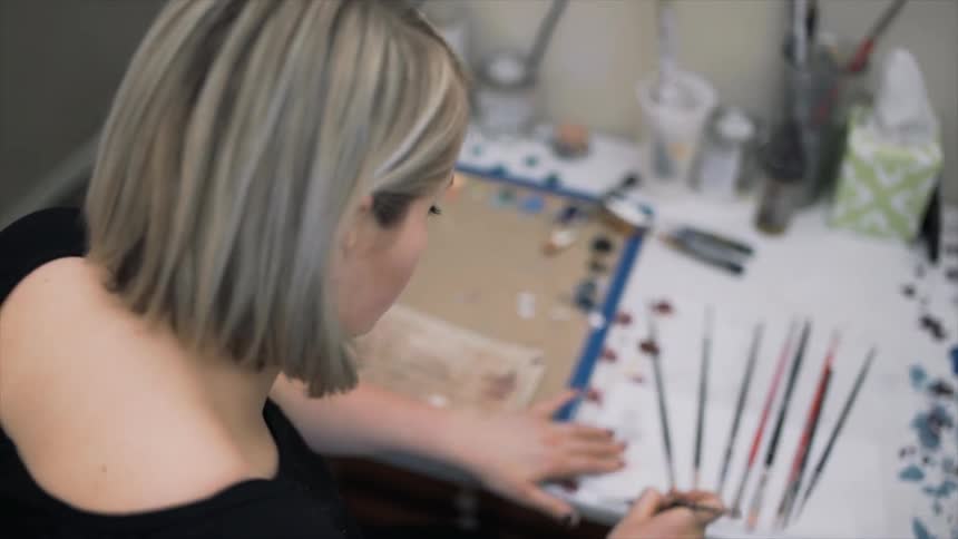 A blond woman sorting paint brushes