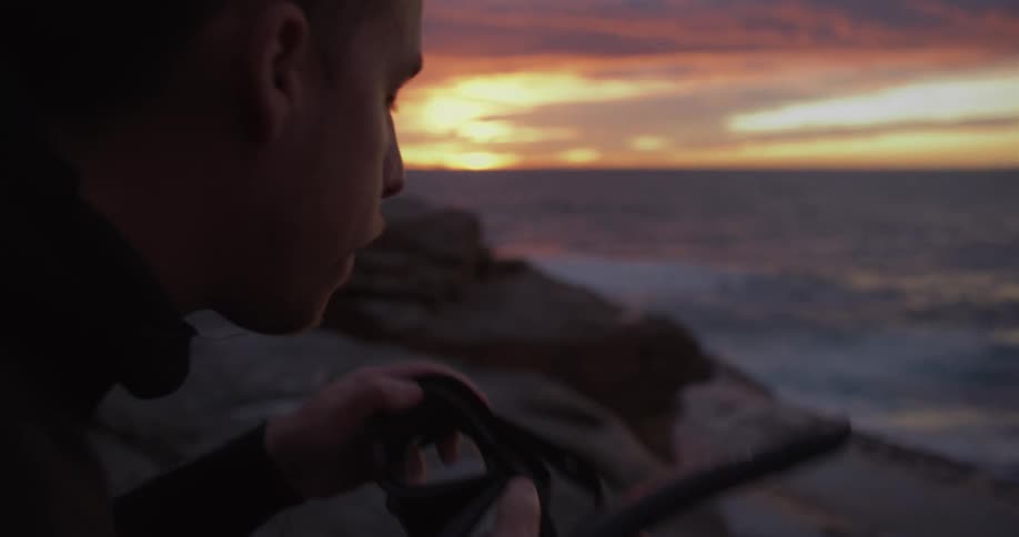A man is standing by the coast of an ocean at dusk