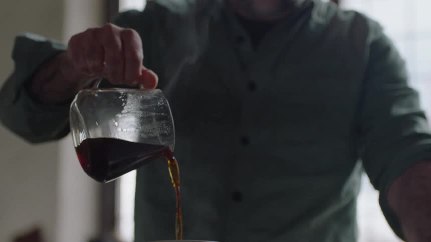 A man pours coffee from a glass coffee pot into a coffee mug