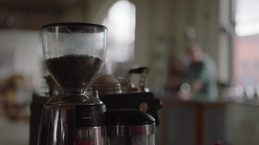 A coffee machine in a room with a person a wall and window in the background