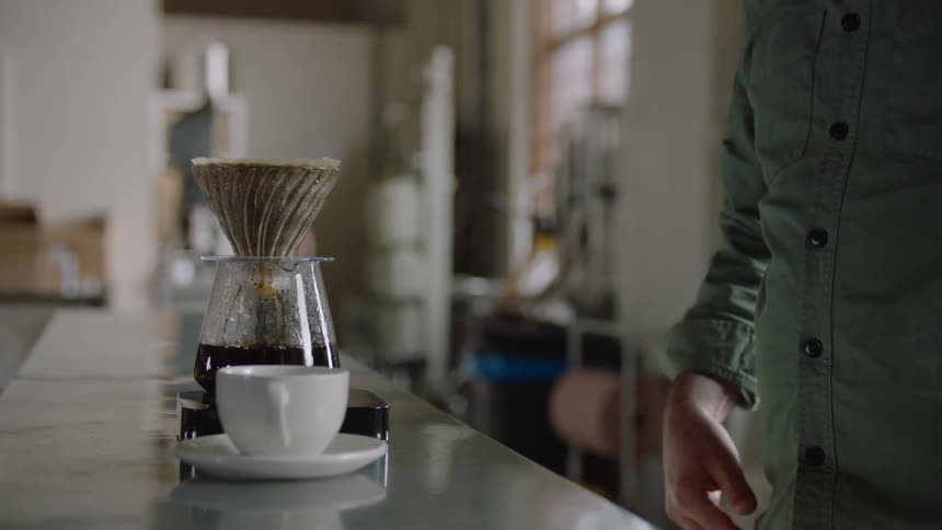 A person in a room with a coffee maker on a counter with a wall and window in the background