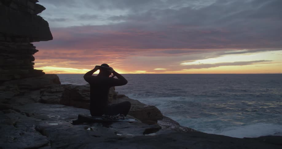 Person dons snorkel mask sitting on rocks near edge of ocean sun turns sky red on the horizon