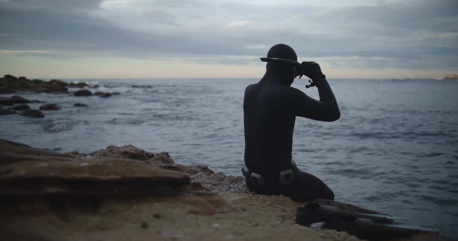 A diver sitting on the coast puts on his snorkel and goggles