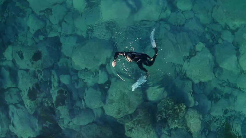 A diver in wet suit swims in the ocean during the day