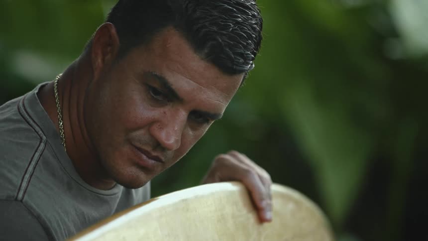 Man stands holding surfboard examining it