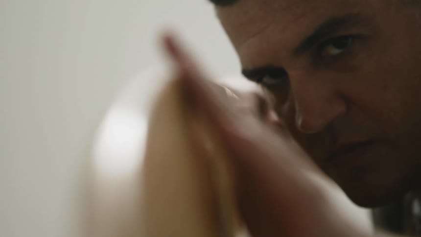 A man in a room examining a surfboard with a wall in the background