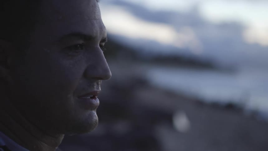 A man sits on the beah at dusk and looks out toward the ocean