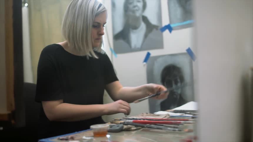 A gray haired woman cleans her paint brushes