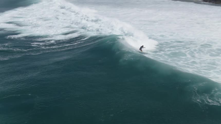 Aerial view of a surfer riding a surfboard on a wave near the coast