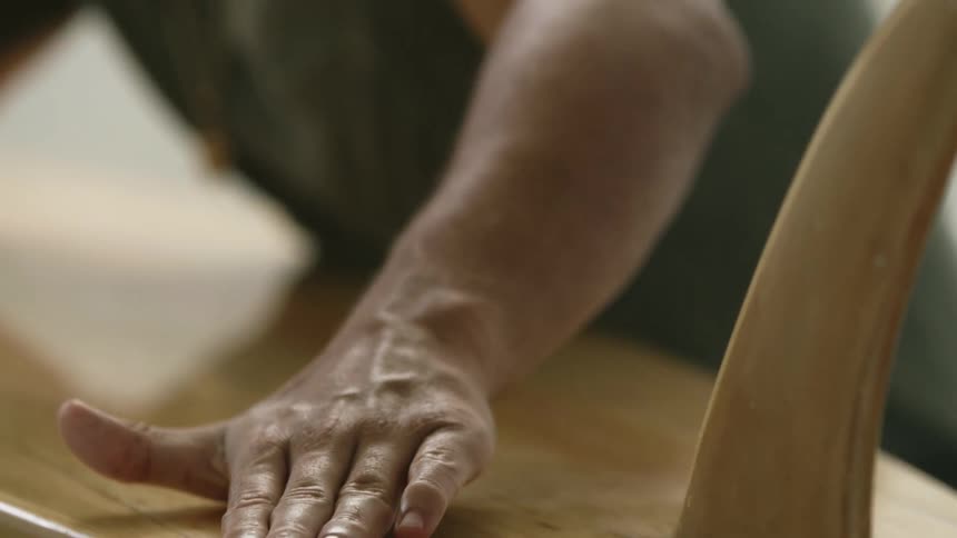 Man strokes hand along bottom of wooden surfboard