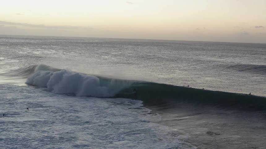 People on surfboards in the ocean with waves with the sky and clouds in the background