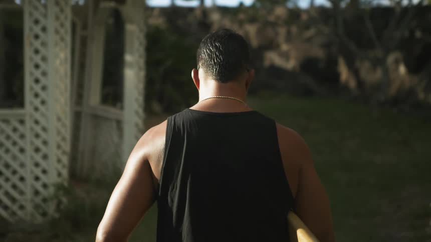 A man is carrying a surfboard through the yard