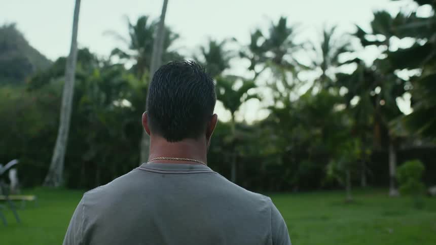 A man walks across a lawn toward some tall trees