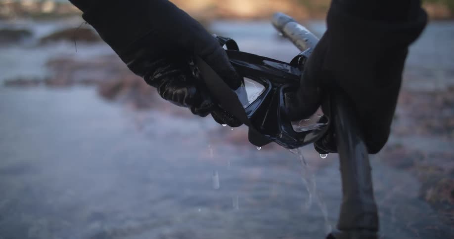 A person with gloves washing a scuba mask in water with the sky and clouds in the background
