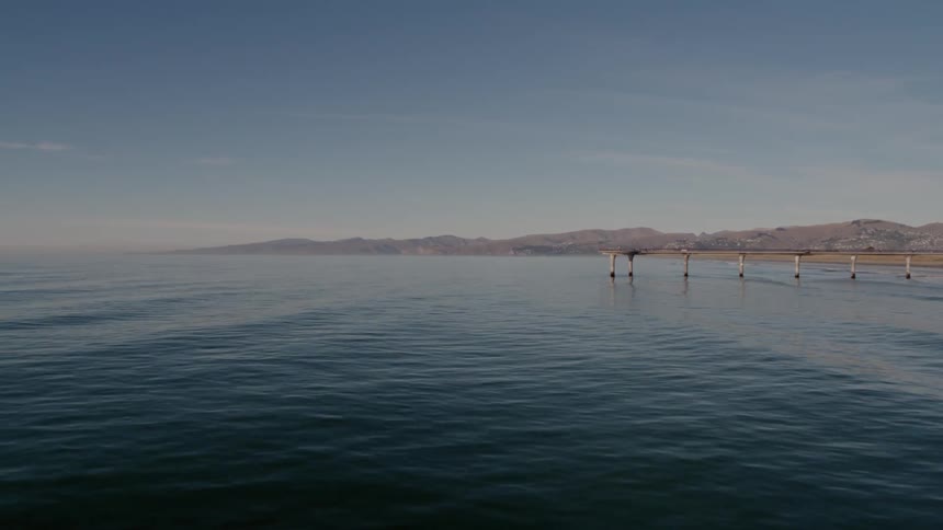 Waves roll in under a dock and onto a beach with mountains on the horizon