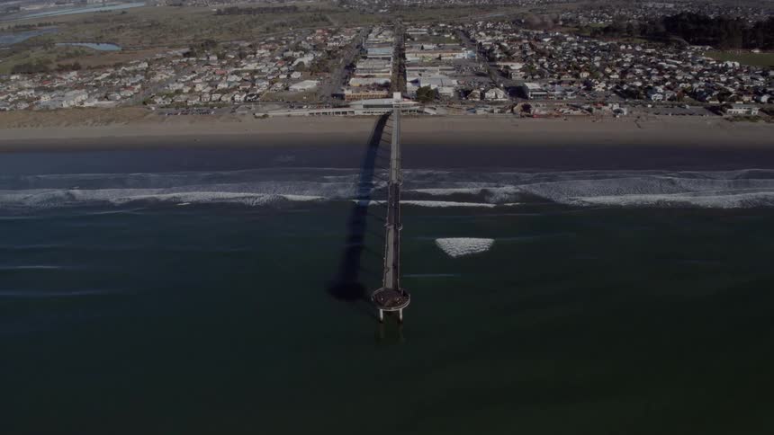 An aerial view of a pier extending into ocean water on a coastline