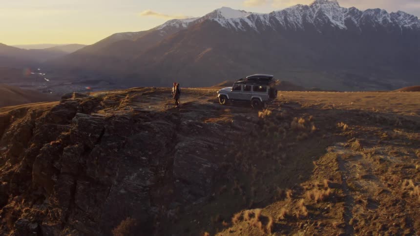 Three people stand near a vehicle and look out at the mountains on a sunny day