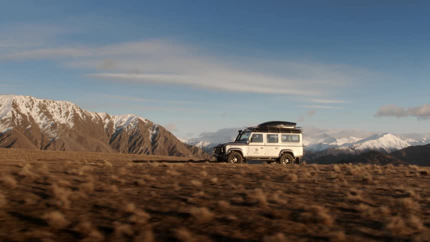 A vehicle drives on a road near snowy mountains