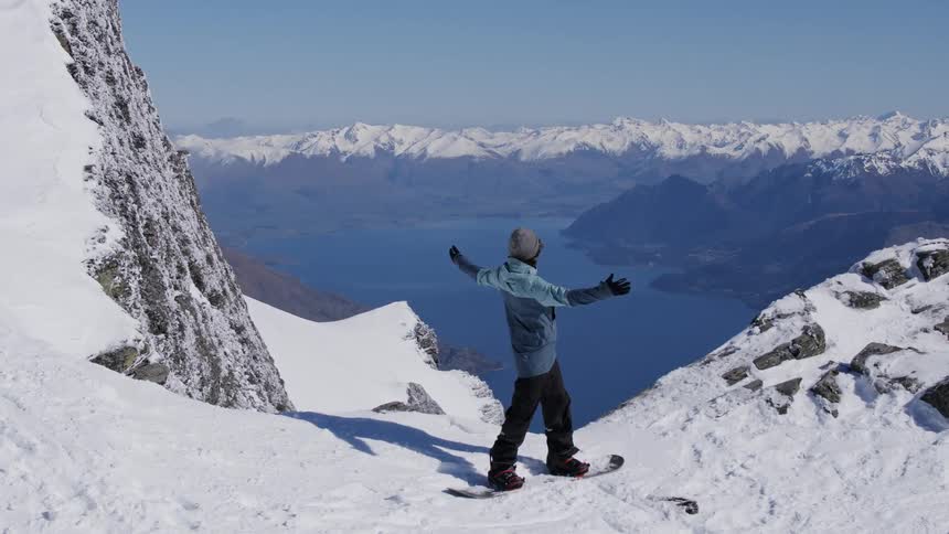 A snowboarder enjoying the view while standing in snowy mountains