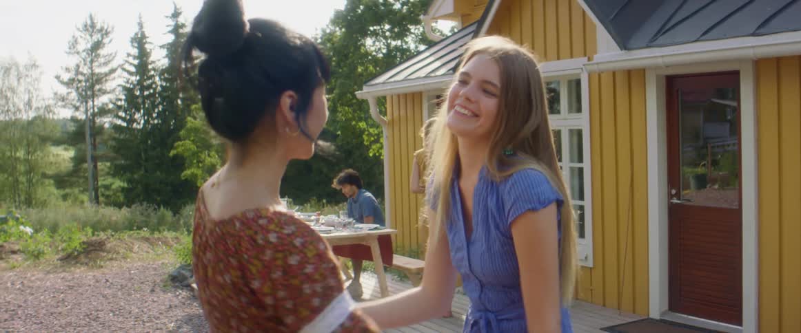 A pair of young women greet each other with a hug and begin chatting