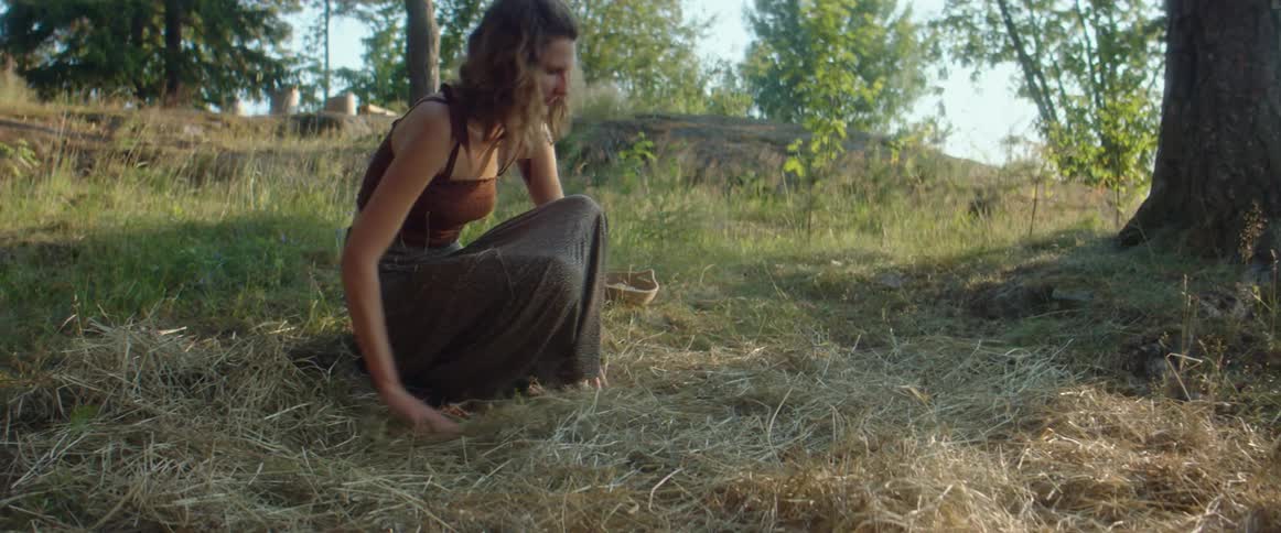 A woman spreading dead grass on the ground outside