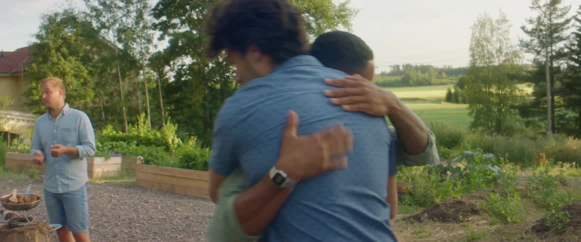 Two men hugging with two women a man trees the sky and clouds in the background