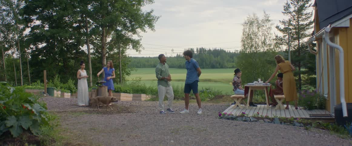 Men and women are outside a farmhouse enjoying conversation with each other