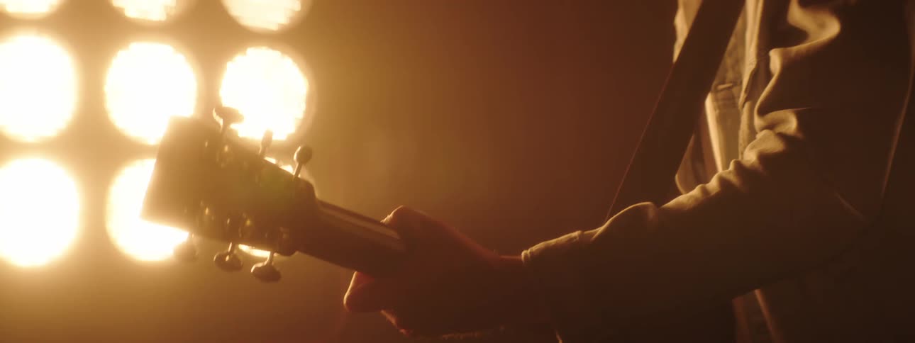 Guitarist playing acoustic guitar on stage in front of flashing yellow lights