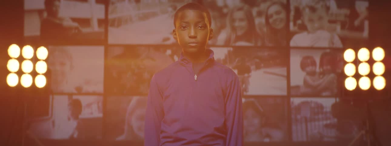 A boy poses in front of a screen showing multiple videos of other children